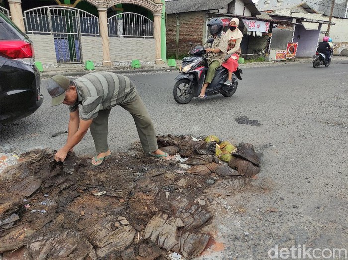 Banyak jalan berlubang di Sidoarjo saat musim hujan. Di Jalan Brigjen Katamso, warga menambal jalan berlubang dengan sabut kelapa.