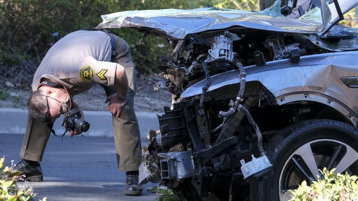 A law enforcement officer looks over a damaged vehicle following a rollover accident involving golfer Tiger Woods, Tuesday, Feb. 23, 2021, in the Rancho Palos Verdes suburb of Los Angeles. Woods suffered leg injuries in the one-car accident and was undergoing surgery, authorities and his manager said. (AP Photo/Ringo H.W. Chiu)
