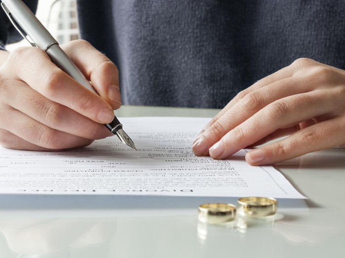Ilustrasi cerai Wife signs divorce decree form with ring
