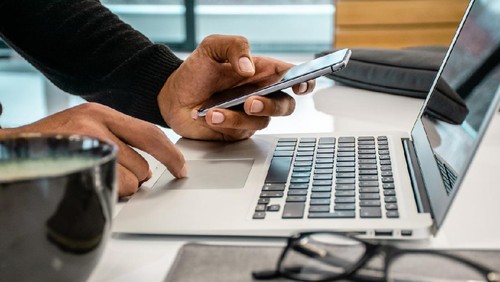 Close up photo of men using phone and laptop in the office