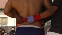 Sebelum pertandingan dimulai, seorang wasit tampak memeriksa ikat pinggang pegulat Naga sebelum mengizinkan dimulainya pertandingan gulat.
