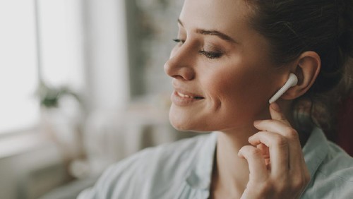 Technology in our life. Close up portrait of young relaxed woman on sofa enjoying of music via wireless earbuds at home