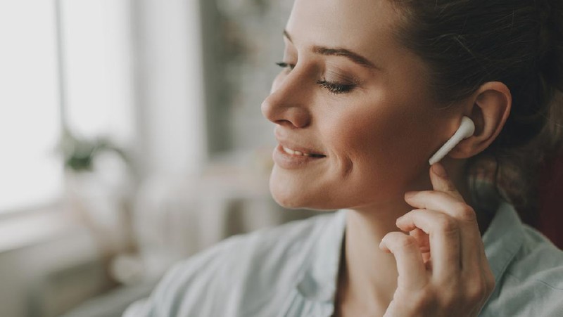 Technology in our life. Close up portrait of young relaxed woman on sofa enjoying of music via wireless earbuds at home