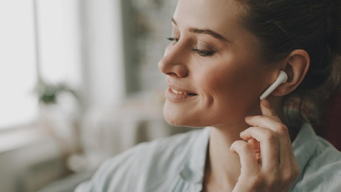 earphone Technology in our life. Close up portrait of young relaxed woman on sofa enjoying of music via wireless earbuds at home