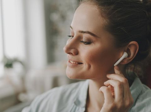 Technology in our life. Close up portrait of young relaxed woman on sofa enjoying of music via wireless earbuds at home