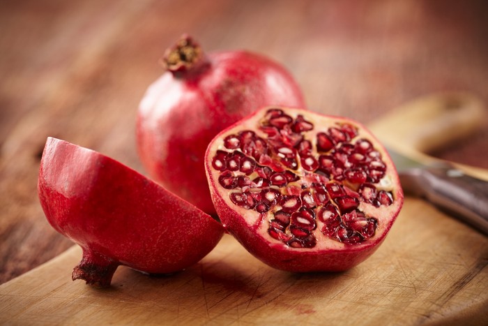 Buah Delima Sliced pomegranate on cutting board with knife and whole pomegranate behind. Shot with shallow focus on sliced fruit.