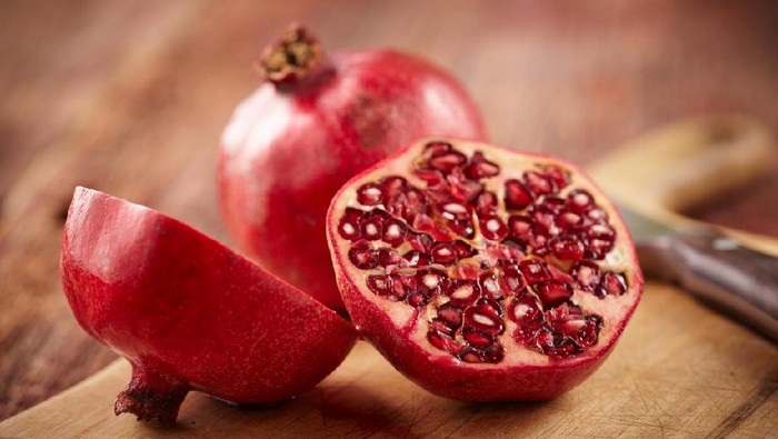 Sliced pomegranate on cutting board with knife and whole pomegranate behind.  Shot with shallow focus on sliced fruit.