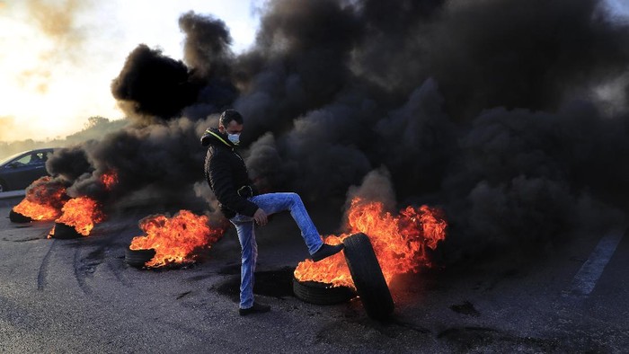 Protesters ride a scooter past burning tires set on fire to block a highway that leads to Beirut's international airport, in Beirut, Lebanon, Tuesday, March 2, 2021. Scattered protests broke out in different parts of Lebanon Tuesday after the Lebanese pound hit a record low against the dollar on the black market, a sign of the country's multiple crises deepening with no prospects for a new Cabinet in the near future. (AP Photo/Hussein Malla)