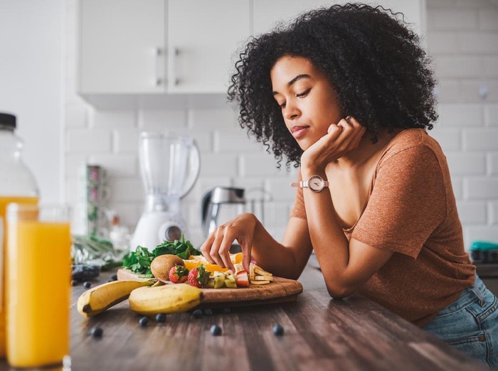 Ilustrasi Diet Shot of a young woman looking unhappy while making a healthy snack with fruit at home