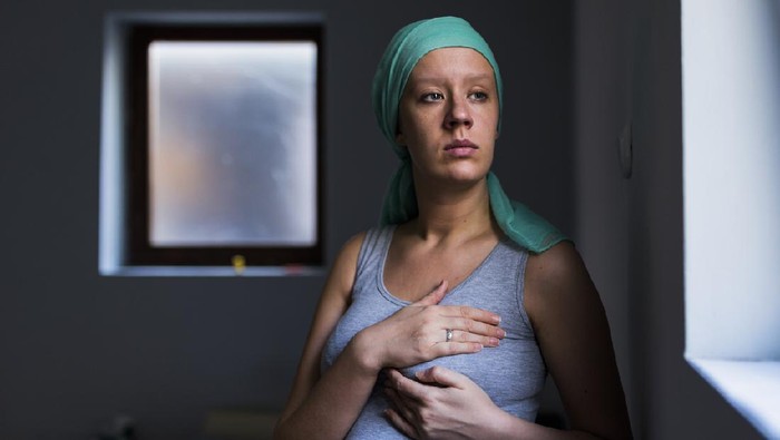 Ilustrasi Tumor Payudara Health, medicine concept - woman in headscarf, fighting breast cancer, checking breast for signs of cancer. Breast examination by home method. Pensive female examining breast at home while standing next to the window during the day.