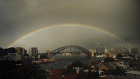 Pelangi dan awan hujan terlihat di atas Jembatan Sydney Harbour di Sydney, Australia. Getty Images/Ryan Pierse