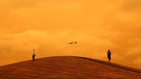 Sebuah pesawat terbang di atas langit yang berwarna oranye akibat kebakaran hutan di Australia. Getty Images/Phil Walter