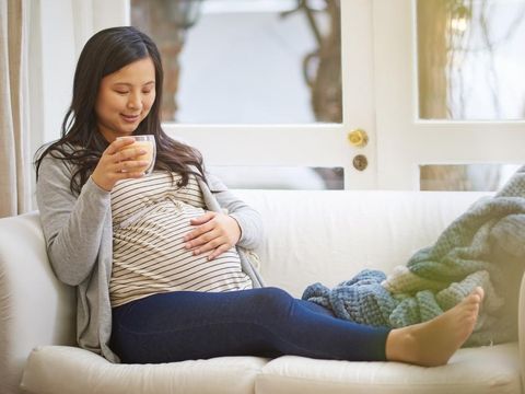 Shot of an attractive young pregnant woman drinking an iced coffee while relaxing on the sofa at home