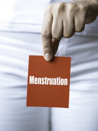 Torso of an unrecognizable woman is showing red square card to camera representing with menstruation written in white.