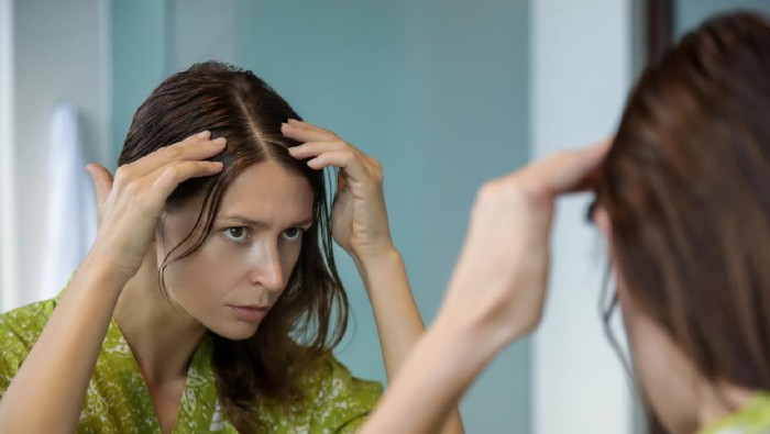 Portrait of a beautiful young woman examining her scalp and hair in front of the mirror, hair roots, color, grey hair, hair loss or dry scalp problem