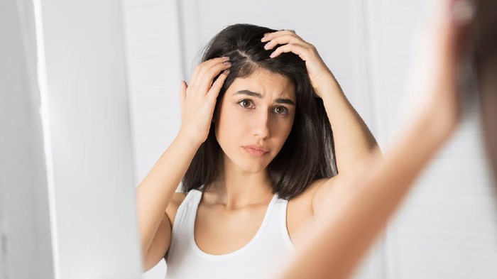 Ilustrasi rambut ketombe Portrait of a beautiful young woman examining her scalp and hair in front of the mirror, hair roots, color, grey hair, hair loss or dry scalp problem