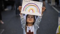 Maria Sole (4) mengenakan pakaian perawat kecil dan memegang gambar pelangi bertuliskan Terima Kasih untuk para tenaga medis. Getty Images/Dan Kitwood