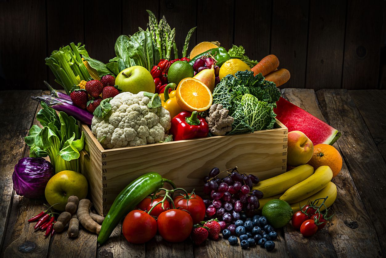 Healthy food: large selection of fresh organic multicolored vegetables in a crate shot on dark wooden table. Fruits and vegetables included in the composition are watermelon, oranges,lime, lemons, banana,grape, strawberries, apples, pears, blueberries, tamarind, kale, tomatoes, squash, asparagus, celery, eggplant, carrots, lettuce, edible mushrooms, bell peppers, cauliflower, ginger, corn, bok choy, raw potatoes, chili peppers among others. High resolution studio digital capture taken with Sony A7rII and Sony FE 90mm f2.8 macro G OSS lens