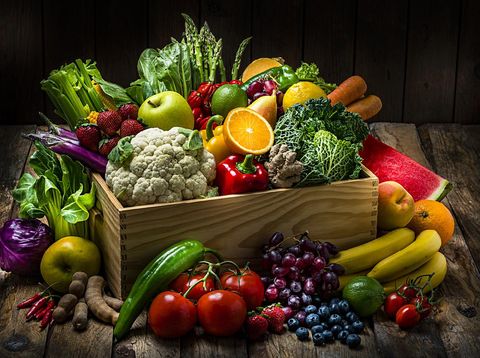 Healthy food: large selection of fresh organic multicolored vegetables in a crate shot on dark wooden table. Fruits and vegetables included in the composition are watermelon, oranges,lime, lemons, banana,grape, strawberries, apples, pears, blueberries, tamarind, kale, tomatoes, squash, asparagus, celery, eggplant, carrots, lettuce, edible mushrooms, bell peppers, cauliflower, ginger, corn, bok choy, raw potatoes, chili peppers among others. High resolution studio digital capture taken with Sony A7rII and Sony FE 90mm f2.8 macro G OSS lens