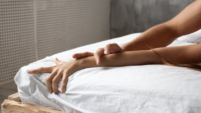 Close up of couple hands lie on bed relaxing in bedroom, lovers have intense sex or making love feeling orgasm and satisfaction, boyfriend and girlfriend enjoy foreplay on white sheets in the morning