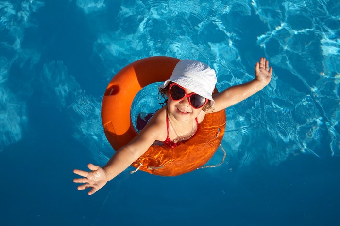 Funny little girl swims in a pool in an orange life preserver