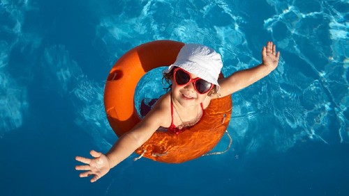 Funny little girl swims in a pool in an orange life preserver
