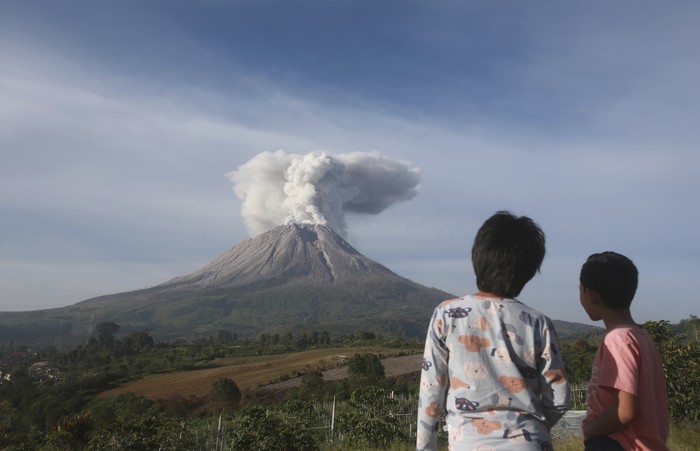 Campers are seen from the opening of a tent as they watch Mount Sinabung erupting in Karo, North Sumatra, Indonesia, Thursday, March 11, 2021. The 2,600-meter (8,530-feet) volcano unleashed an avalanche of searing gas clouds flowing down its slopes during eruption on Thursday. No casualties were reported. (AP Photo/Binsar Bakkara)