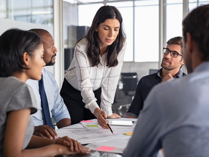 Team of multiethnic architects working on construction plans in meeting room. Engineers and designers discussing project in office. Businesswoman with business team in conference room working on blueprint.