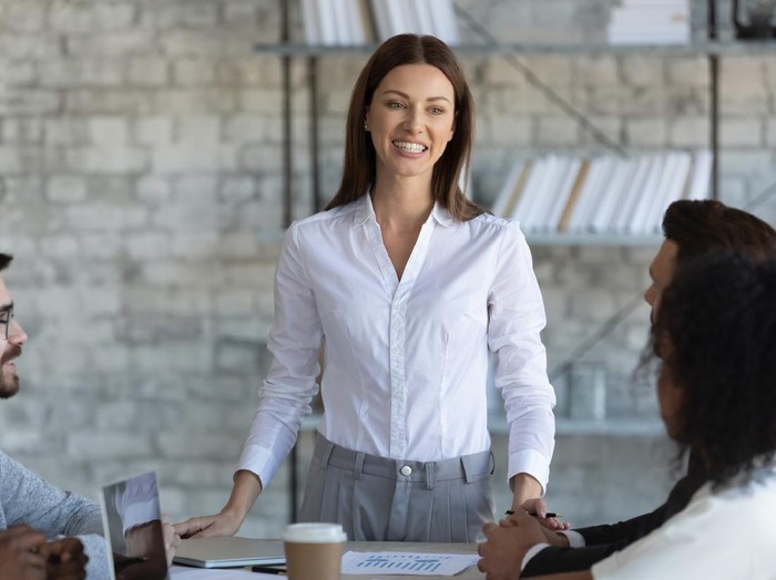 Happy businesswoman manager speaks in boardroom at meeting. Female mentor coach lead presentation new project for colleagues in conversation at negotiation. Woman employee communicating with partners.