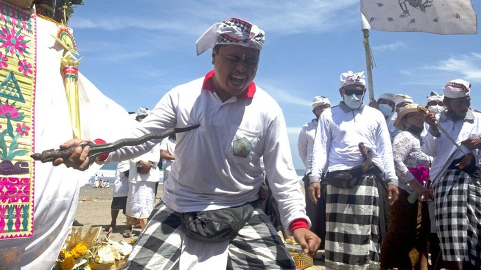 A man points keris, traditional daggers, to his chest during the ritual of Melasti in Bali, Indonesia, Thursday, March 11, 2021. The ritual, which is performed ahead of the Balinese Hindus Day of Silence, is held to purify the universe from bad influences, bad deeds and bad thoughts. (AP Photo/Firdia Lisnawati)