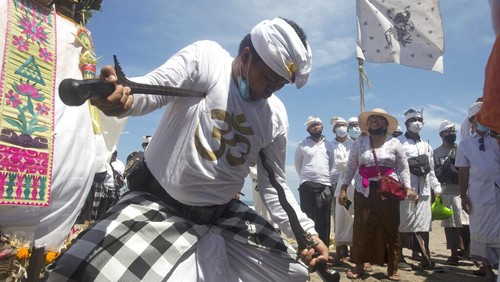 A man points keris, traditional daggers, to his chest during the ritual of Melasti in Bali, Indonesia, Thursday, March 11, 2021. The ritual, which is performed ahead of the Balinese Hindus Day of Silence, is held to purify the universe from bad influences, bad deeds and bad thoughts. (AP Photo/Firdia Lisnawati)