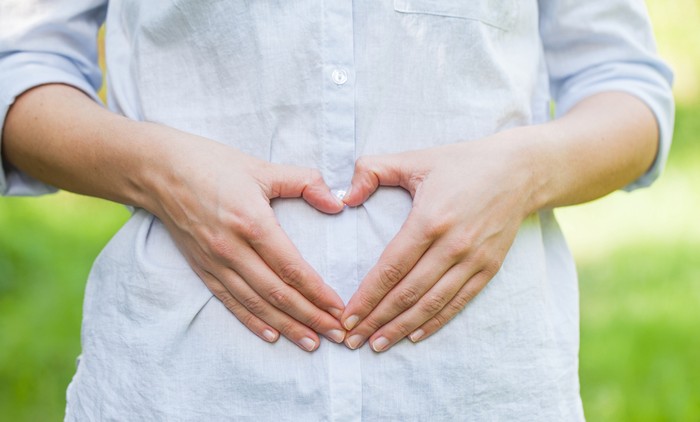 Close up picture of a pregnant woman showing a love sign on her belly in the first trimester, outdoor