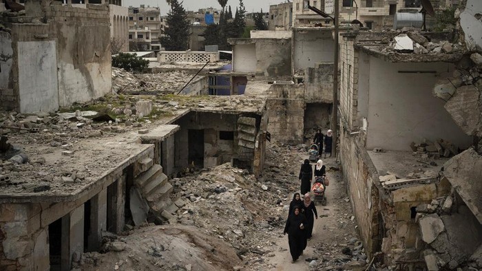 FILE - In this March 12, 2020 file photo, women walk in a neighborhood heavily damaged by airstrikes in Idlib, Syria. Hundreds of thousands of Syrians face continued displacement each coming year if the conflict continues and economic conditions further deteriorate, the Norwegian Refugee Council, a prominent humanitarian organization said Monday, March 8, 2021. The Syrian conflict, which marks 10 years later this month, has resulted in the largest displacement crisis since World War II, with an estimated 2.4 million people displaced in and outside Syria every year since the war begin in 2011, the council said. (AP Photo/Felipe Dana, File)