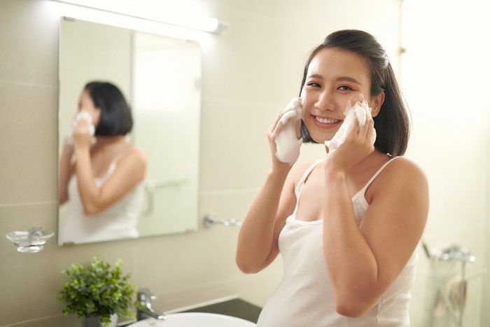 Pregnant woman splashing face with water above bathroom sink