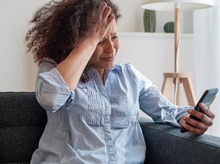 1222038503 Sad black woman reading bad news on mobile phone