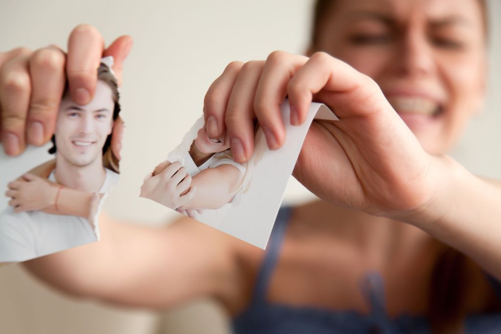 Close up image of torn into two pieces photograph of happy smiling and hugging young couple in hands of upset crying woman angry because of divorce or breakup of relations. Betrayal, jealousy concept