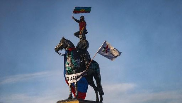 (FILES) In this file photo taken on October 03, 2020, a demonstrator holds a Mapuche flag a top an equestrian sculpture of Chilean former Commander-in-chief of the Army, Manuel Baquedano, during a protest against the Chilean police after Antony Araya, 16, fell from a bridge while police was attempting to arrest him during Friday clashes, at Plaza Italia square in Santiago. - The statue of General Manuel Baquedano in Santiagos Plaza Italia, vandalised every week in the most radical protests, was removed on March 12, 2021 amid a symbolic battle for control of the place that concentrates social demonstrations in Chile. (Photo by JAVIER TORRES / AFP)