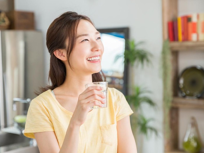 young attractive asian woman who drinks water in a kitchen