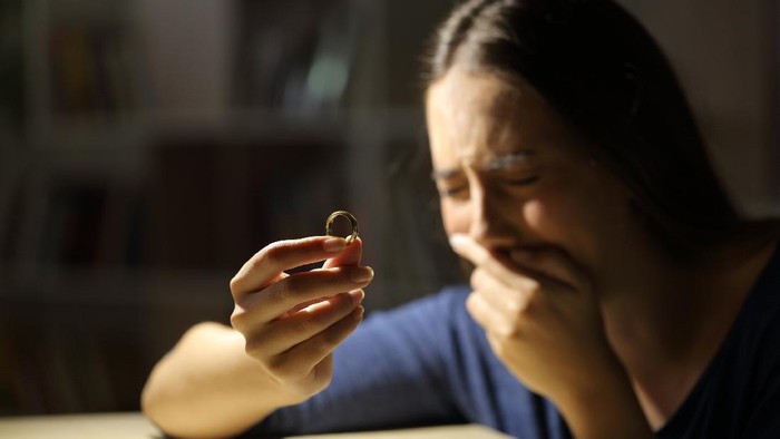 Sad wife crying hoding wedding ring in the night at home