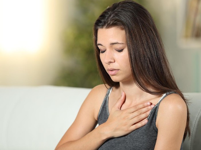 1214455854 Girl having respiration problems touching chest sitting on a couch in the living room at home