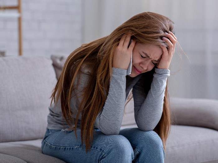 1285255535 Sad young woman having conversation on mobile phone and crying at home. Millennial lady having difficult talk, hearing sad news, going through breakup or relationship problems