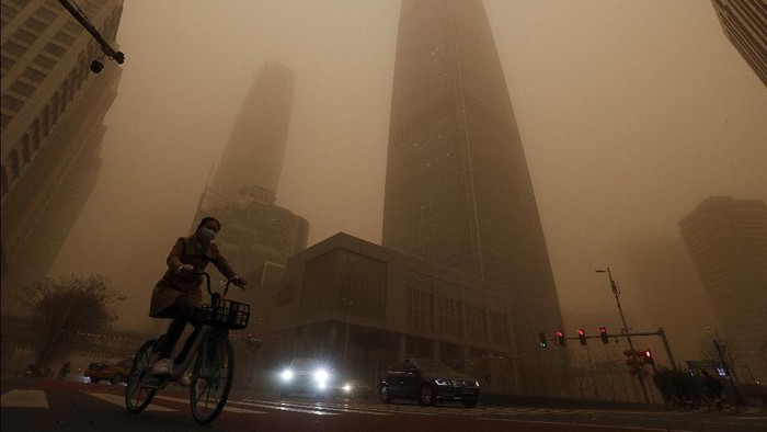 Gegara Badai Pasir, China Diselimuti Kabut Kuning Berbahaya A cyclist and motorists move past office buildings amid a sandstorm during the morning rush hour in the central business district in Beijing, Monday, March 15, 2021. The sandstorm brought a tinted haze to Beijing's skies and sent air quality indices soaring on Monday. (AP Photo/Andy Wong)