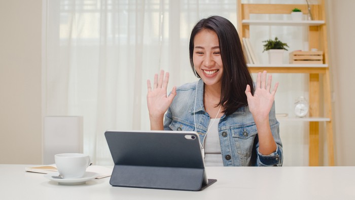 mengajar online Freelance business women casual wear using tablet working call video conference with customer in workplace in living room at home. Happy young Asian girl relax sitting on desk do job in internet.