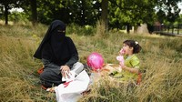 Seorang ibu Muslim memakai burka duduk santai bersama anaknya di taman di Kota London, Inggris, dalam perayaaan Idul Fitri Agustus 2013. Dan Kitwood/Getty Images.