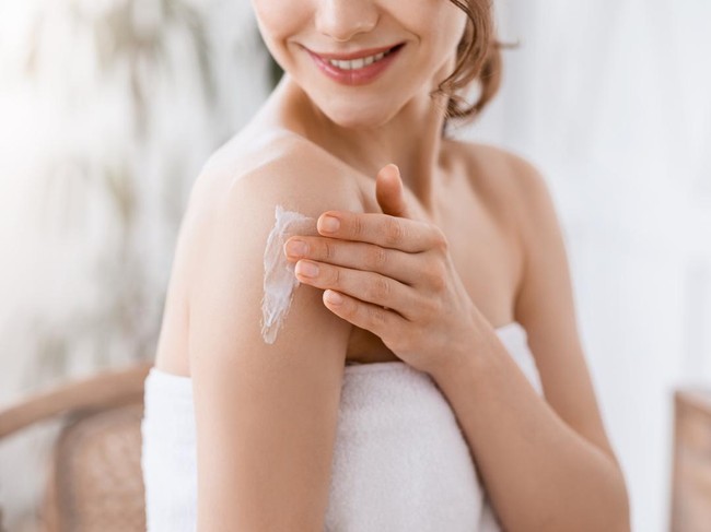 Dry Elbows Treatment. Smiling Black Woman Applying Moisturising Cream At Home, Healing Cracked Skin