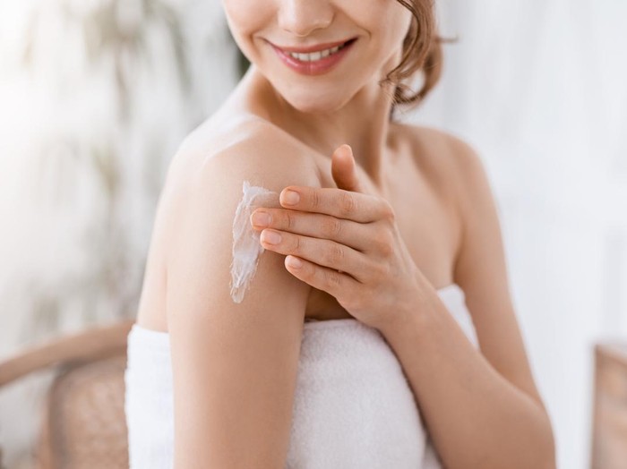 Dry Elbows Treatment. Smiling Black Woman Applying Moisturising Cream At Home, Healing Cracked Skin
