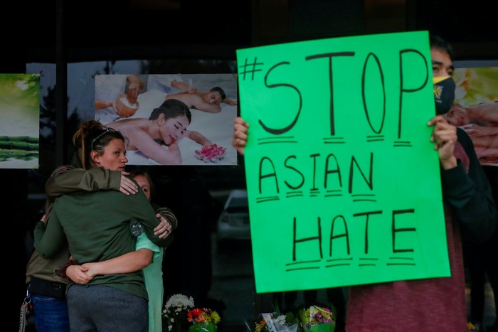 People grieve while Jesus Estrella, 21 holds a sign outside Youngs Asian Massage following the deadly shootings in Acworth, Georgia, U.S. March 17, 2021. REUTERS/Shannon Stapleton  REFILE - CORRECTING NAME OF SPA     TPX IMAGES OF THE DAY