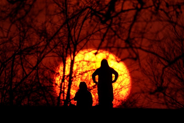 Girls are silhouetted against the setting sun as they enjoy a spring-like day Saturday, March 6, 2021, in Kansas City, Mo.