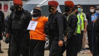 Masing-masing tersangka tampak dikawal dua anggota Densus 88 di kedua sisinya saat turun dari pesawat. Di belakang, satu orang anggota Densus 88 dengan senjata lengkap mengikuti.