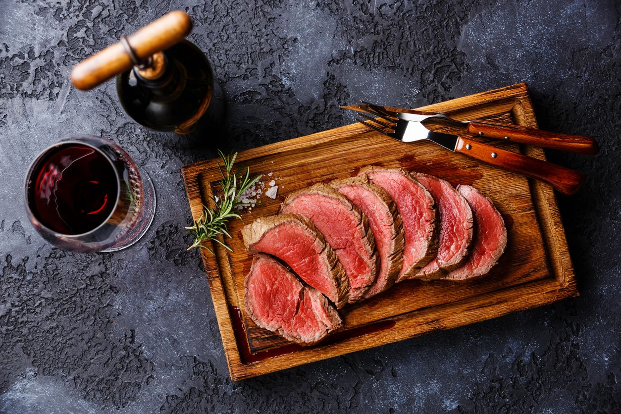 Sliced grilled tenderloin Steak roastbeef on wooden cutting board and Red wine on dark background